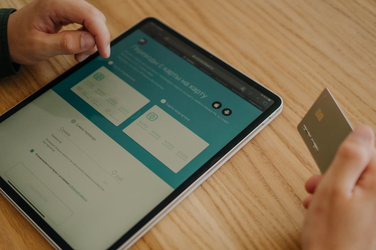 Hands making an online purchase using a tablet and credit card on a wooden table.