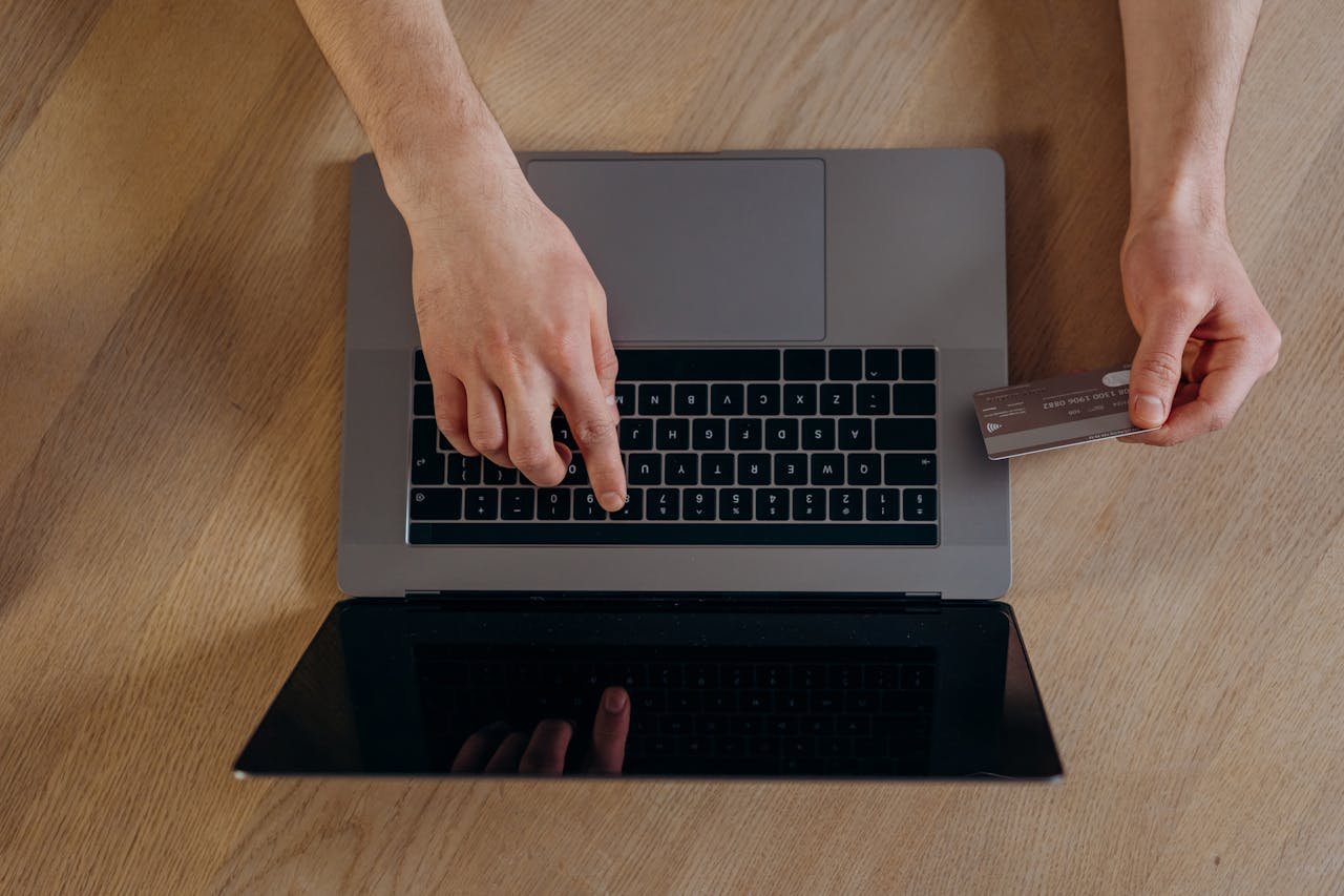 Top view of hands using a credit card and laptop for online transactions on a wooden surface.